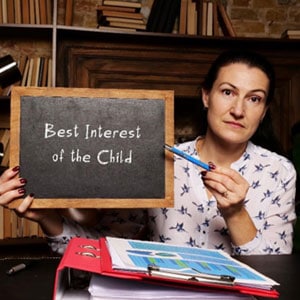 A woman holds a blackboard with the words "best interest of the child" written on it